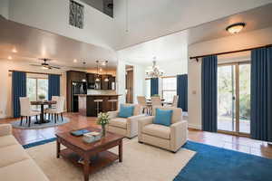 Living room featuring light tile patterned floors, ceiling fan with notable chandelier, a wealth of natural light, and a high ceiling