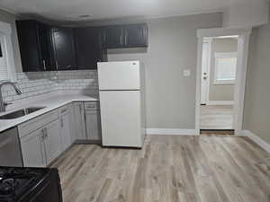 Kitchen with white fridge, light hardwood / wood-style flooring, backsplash, stainless steel dishwasher, and sink