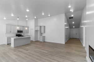 Kitchen featuring light wood-type flooring, pendant lighting, high vaulted ceiling, stainless steel appliances, and an island with sink