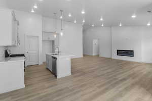 Kitchen featuring hanging light fixtures, backsplash, white appliances, light hardwood / wood-style floors, and an island with sink