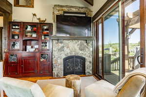 Living room featuring a stone fireplace, lofted ceiling with beams, and light wood-type flooring