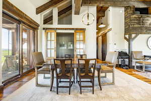 Dining space with beam ceiling, wood-type flooring, high vaulted ceiling, and a chandelier