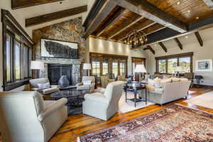 Living room featuring lofted ceiling with beams, hardwood / wood-style flooring, wooden ceiling, a fireplace, and a chandelier