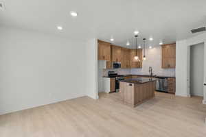 Kitchen featuring decorative light fixtures, appliances with stainless steel finishes, a center island, and light wood-type flooring