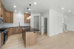 Kitchen featuring backsplash, decorative light fixtures, a kitchen island, appliances with stainless steel finishes, and light hardwood / wood-style floors