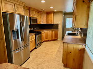 Kitchen with backsplash, appliances with stainless steel finishes, sink, and light tile floors