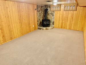 Basement featuring carpet floors, wood walls, and a wood stove