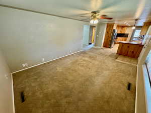 Unfurnished living room with light colored carpet, sink, and ceiling fan