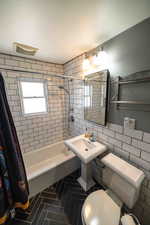 Bathroom with shower / bath combo with shower curtain, tile flooring, toilet, and tile walls