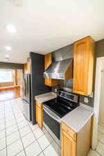 Kitchen featuring wall chimney exhaust hood, stainless steel appliances, and light tile floors