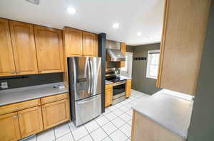 Kitchen with stainless steel appliances, wall chimney exhaust hood, and light tile flooring