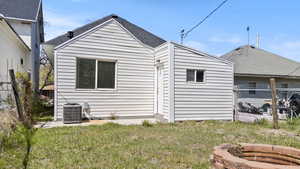 Back of property featuring central AC unit, roof with shingles, fence, and a yard