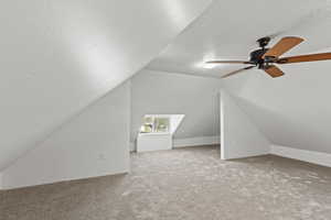 Bonus room with vaulted ceiling, carpet flooring, a textured ceiling, and ceiling fan