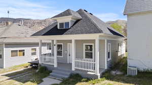 View of front facade featuring central air condition unit, a shingled roof, a porch, and a mountain view