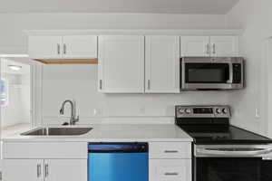 Kitchen featuring light stone counters, appliances with stainless steel finishes, white cabinetry, and a sink