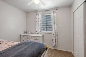 Carpeted bedroom featuring ceiling fan and a closet