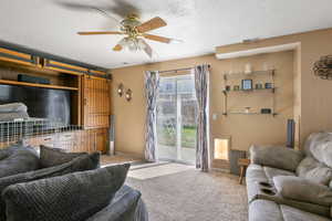 Carpeted living room featuring a barn door, a textured ceiling, and ceiling fan