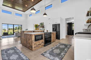 Kitchen with black appliances, a kitchen island, hanging light fixtures, a towering ceiling, and wooden ceiling