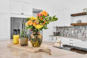 Room details featuring white cabinets, tasteful backsplash, and stainless steel fridge with ice dispenser