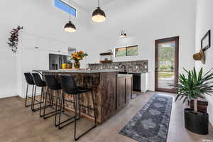 Bar with a towering ceiling, tasteful backsplash, concrete floors, stainless steel fridge, and pendant lighting