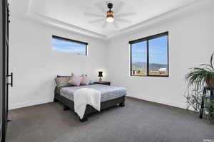 Bedroom featuring dark carpet, ceiling fan, and a raised ceiling