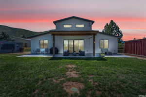 Back house at dusk with a yard, outdoor lounge area, and a patio area