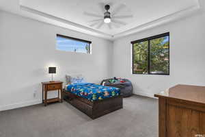 Bedroom with a raised ceiling, ceiling fan, and carpet floors