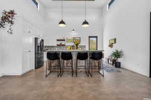 Kitchen featuring a kitchen breakfast bar, a towering ceiling, concrete floors, and stainless steel refrigerator with ice dispenser