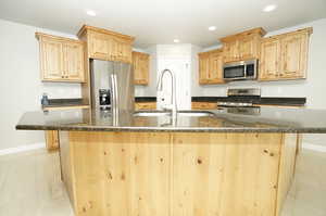 Kitchen featuring an island with sink, stainless steel appliances, and light brown cabinetry