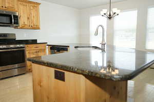 Kitchen with dark stone counters, appliances with stainless steel finishes, hanging light fixtures, sink, and a chandelier