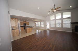 Unfurnished living room with high vaulted ceiling, hardwood / wood-style floors, a stone fireplace, and ceiling fan