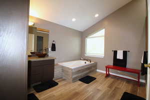 Bathroom featuring vaulted ceiling, vanity, a tub, and wood-style floors