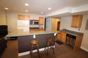 Kitchen featuring white fridge, a kitchen breakfast bar, stainless steel microwave, a center island, and sink