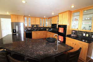 Kitchen with dark granite countertops, wood-style floors, tasteful backsplash, and a center island