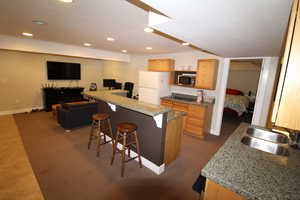 Kitchen featuring white fridge, a kitchen breakfast bar, stainless steel microwave, a center island, and sink