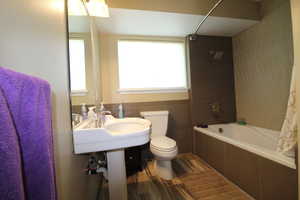 Bathroom featuring wood-style floors, toilet, shower/bath combo with shower curtain, and tile walls