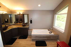 Bathroom with a wealth of natural light, vaulted ceiling, tiled tub, and oversized vanity