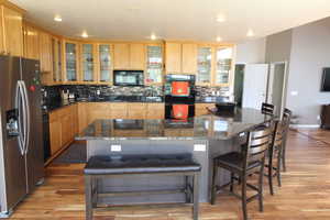 Kitchen with dark granite countertops, wood-style floors, tasteful backsplash, and a center island