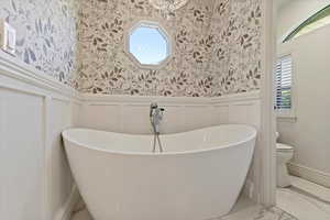 Bathroom featuring a healthy amount of sunlight, a tub, toilet, and tile floors