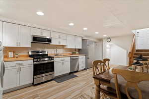 Basement Kitchen with light hardwood / wood-style flooring, white cabinets, and appliances with stainless steel finishes