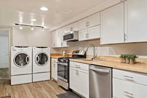 Basement Kitchen featuring washer and dryer, butcher block counters, light hardwood / wood-style flooring, appliances with stainless steel finishes, and white cabinets