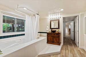 Bathroom featuring wood-type flooring, tiled bath, a textured ceiling, and large vanity