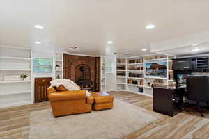 Basement Family room with brick wall, built in features, a wood stove, and light hardwood / wood-style flooring