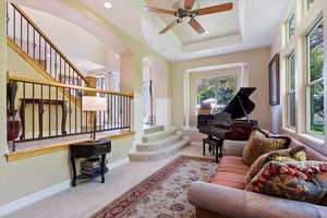 Carpeted living room featuring a high ceiling, ceiling fan, and a tray ceiling