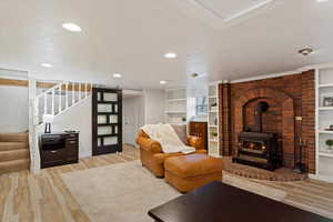 Basement Family Room featuring built in shelves, light wood-type flooring, a wood stove, and brick wall