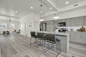 Kitchen featuring a kitchen breakfast bar, an island with sink, light wood-type flooring, hanging light fixtures, and appliances with stainless steel finishes