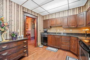 Kitchen featuring dark stone counters, light hardwood / wood-style floors, black dishwasher, range, and sink