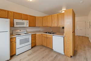 Kitchen featuring white appliances, sink, and light wood-type flooring