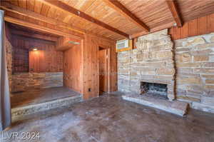 Unfurnished living room with a stone fireplace, wooden walls, beamed ceiling, and wood ceiling