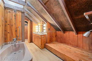 Bathroom featuring hardwood / wood-style floors, wooden walls, vanity, and lofted ceiling with skylight